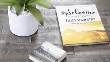 A welcome book, a potted plant, and a stack of brochures on a wooden surface.