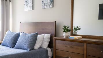 A bedroom with a bed, two pillows, a nightstand with a plant, and a mirror.