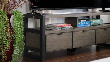 A modern entertainment unit with a flat-screen TV, a red vase with green plants, and a few books.