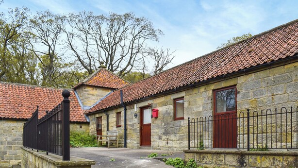 A stone building with a tiled roof, a wooden bench, and a metal fence. - Beech Cottage - UK49564 (Sneaton, near Whitby)