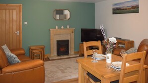 A living room with a fireplace, a television, a dining table with chairs, and a sofa. - Beech Cottage - UK49564 (Sneaton, near Whitby)