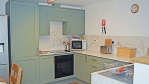 A kitchen with green cabinets, a microwave, a toaster, and a clock on the wall. - Beech Cottage - UK49564 (Sneaton, near Whitby)