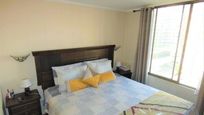 A neatly made bed with a patterned bedspread, a nightstand with a lamp, and a window with curtains. - Special for business, 2 blocks from the subway! (Ñuñoa)