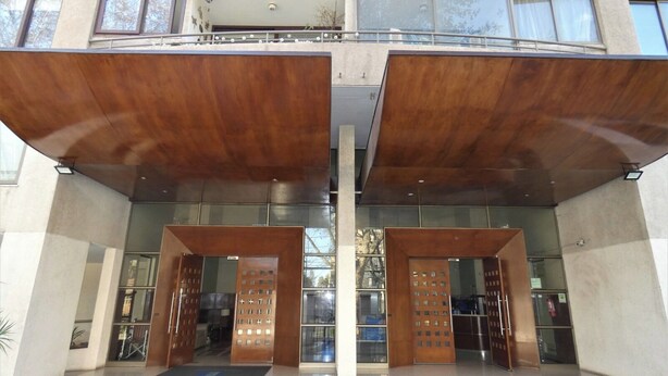 A modern building with a symmetrical facade, large glass windows, and a central entrance with wooden doors and a metal gate. - Special for business, 2 blocks from the subway! (Ñuñoa)