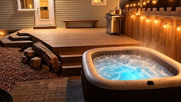 Un bain à remous sur une terrasse en bois, avec un banc et un barbecue.