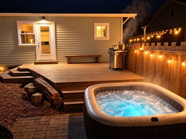 A hot tub on a wooden deck with a bench and a grill.
