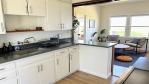 A modern kitchen with white cabinets, a black countertop, and a built-in stove. There is a dining area with a round table and chairs, and a rug on the floor.