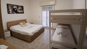 Een slaapkamer met een houten bed, een stapelbed, een nachtkastje, een kunstwerk aan de muur en een raam met gordijnen.