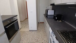 Een functionele keuken met een inbouwoven, een magnetron, een koffiezetapparaat en een wasmachine.