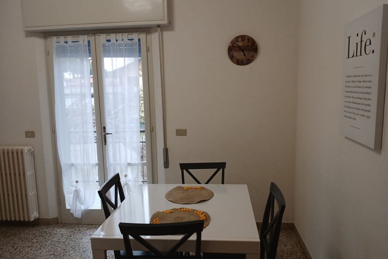 A dining area with a white table, two black chairs, a clock on the wall, and a door with a curtain.