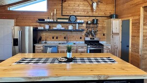 Een rustieke keuken met houten wanden, een grote houten tafel en een opgehangen hertenschedel.