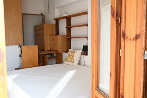 A bedroom with a bed, wooden dresser, shelves, and a window.