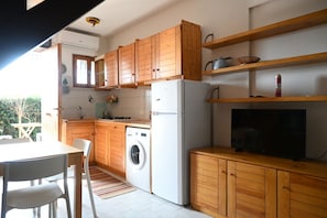 A compact kitchen with wooden cabinets, a washing machine, a refrigerator, and a television.