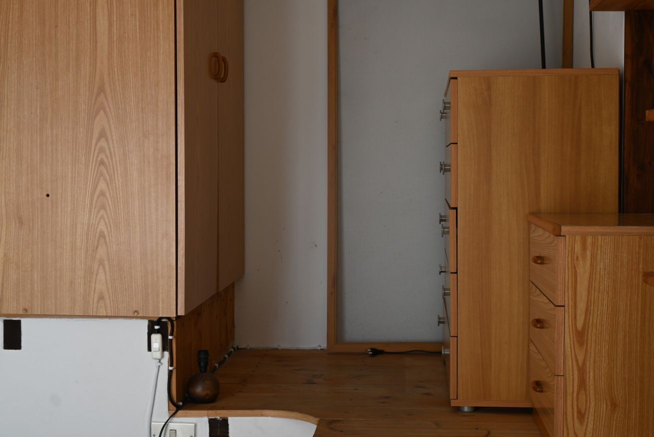 Une pièce avec des armoires en bois, un mur blanc et une porte.