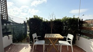 A patio with a wooden table and white chairs, surrounded by a brick floor and a hedge. -  M419 – Marcelli, one bedroom apartment eith terrace and air conditioning (Marcelli)