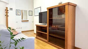 Ein Wohnzimmer mit einer Couch, einem Fernseher auf einem Holzboden, einer Vitrine und gerahmten Bildern an der Wand.