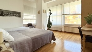 Ein Schlafzimmer mit Bett, Schreibtisch, Stuhl, einem Fenster mit Blick und einer Kakteepflanze.
