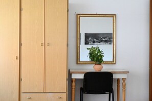 Huoneessa on puinen vaatekaappi, pöytä, jonka päällä on kehystetty kuva, ja ruukussa oleva kasvi.