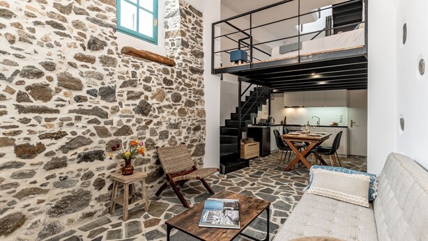 A cozy interior with a stone wall, a wooden chair, a sofa, and a dining area with a staircase. - The Naxos Loft with view of the Castle (Naxos)