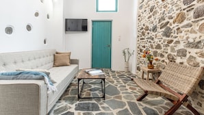 A room with a stone floor, a teal door, a white sofa, a wooden coffee table, and a wicker chair. - The Naxos Loft with view of the Castle (Naxos)