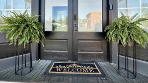 A dark wooden double door with a 'WELCOME' mat at the entrance. - Katy Suite - Chic 2BR Stay on Katy Trail in Historic Mercantile near Hermann (Hermann)