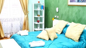 Une chambre avec une couvre-lit bleue, des oreillers blancs et un banc blanc. Un mur est peint en vert et un tableau est accroché au-dessus du lit.