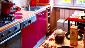 Une cuisine avec des meubles de rangement rouges, une cuisinière, un évier et une fenêtre ornée de rideaux jaunes.