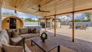 A covered outdoor living area with a wooden ceiling, a built-in hot tub, a barbecue grill, and a seating area with a sofa and coffee table.