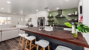 A modern kitchen with a central island, bar stools, and a dining area with a sofa.