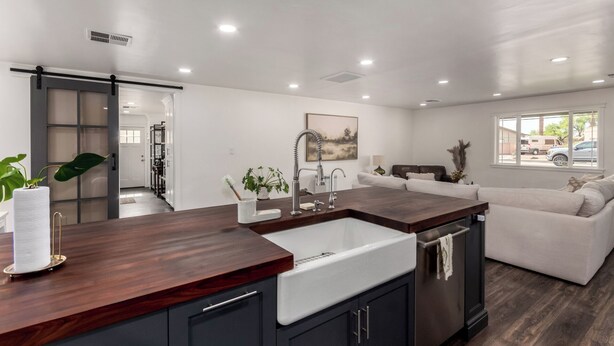 A modern kitchen with dark wood countertops, a white sink, and dark cabinets. There is a sliding glass door leading to a hallway.