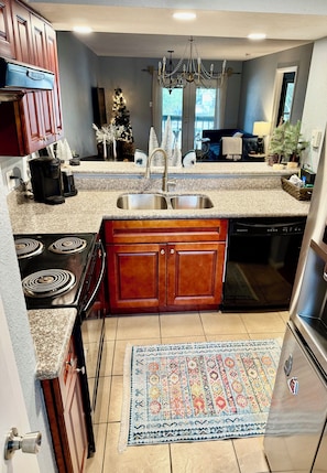 A kitchen with granite countertops, wooden cabinets, a built-in dishwasher, a double sink, a stove, and a chandelier.