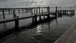 Eine Holzstege streckt sich ins ruhige Wasser, über ihm ein bewölkter Himmel.