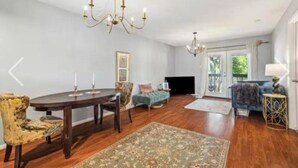 Ein geräumiges Wohnzimmer mit einem runden Holztisch, zwei Stühlen, einem Sofa, einem blauen Ohrensessel, einem Teppich mit Muster und zwei Kronleuchtern.