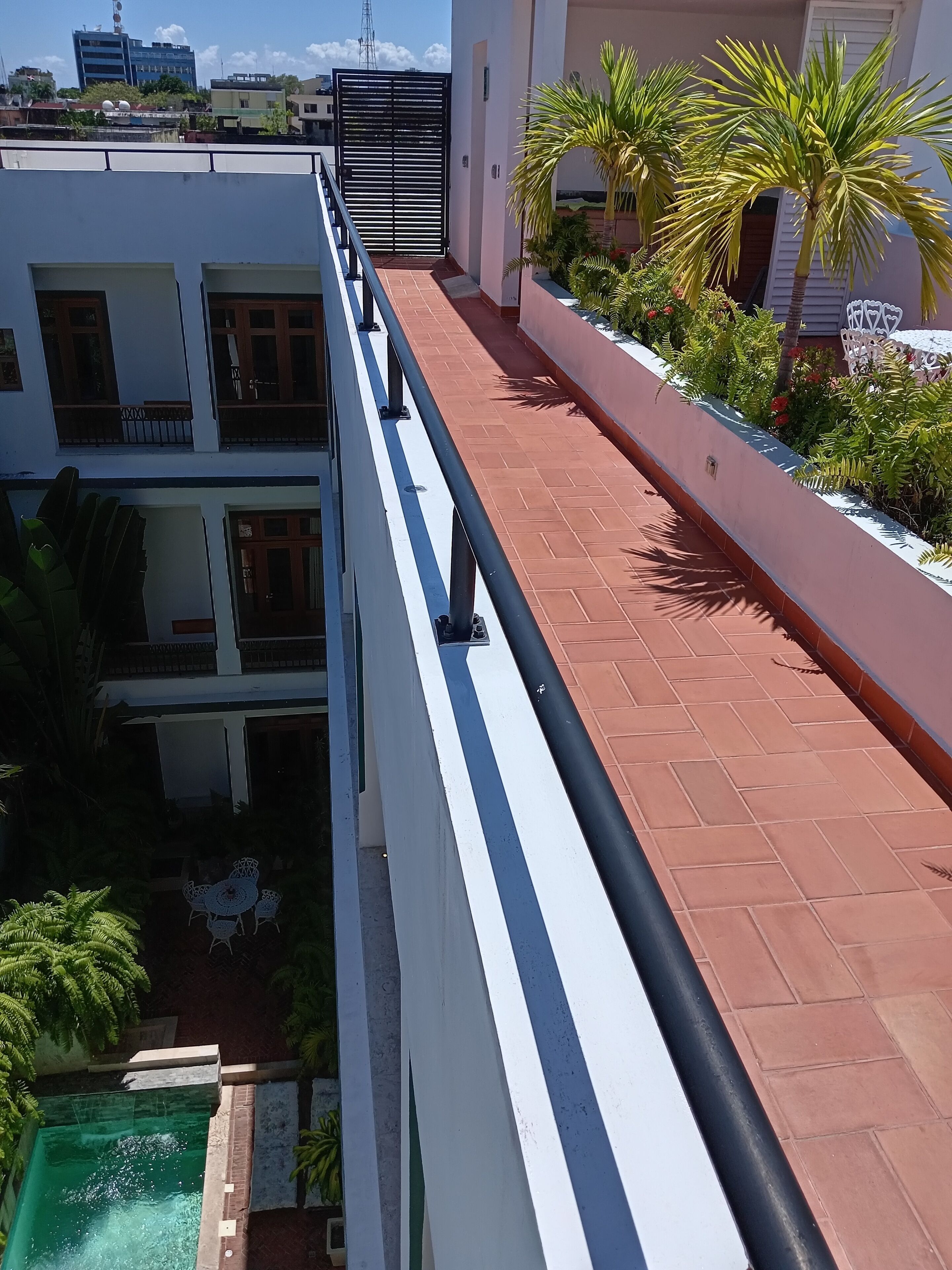 A multi-story building with a rooftop terrace, a swimming pool, and a garden area with palm trees.