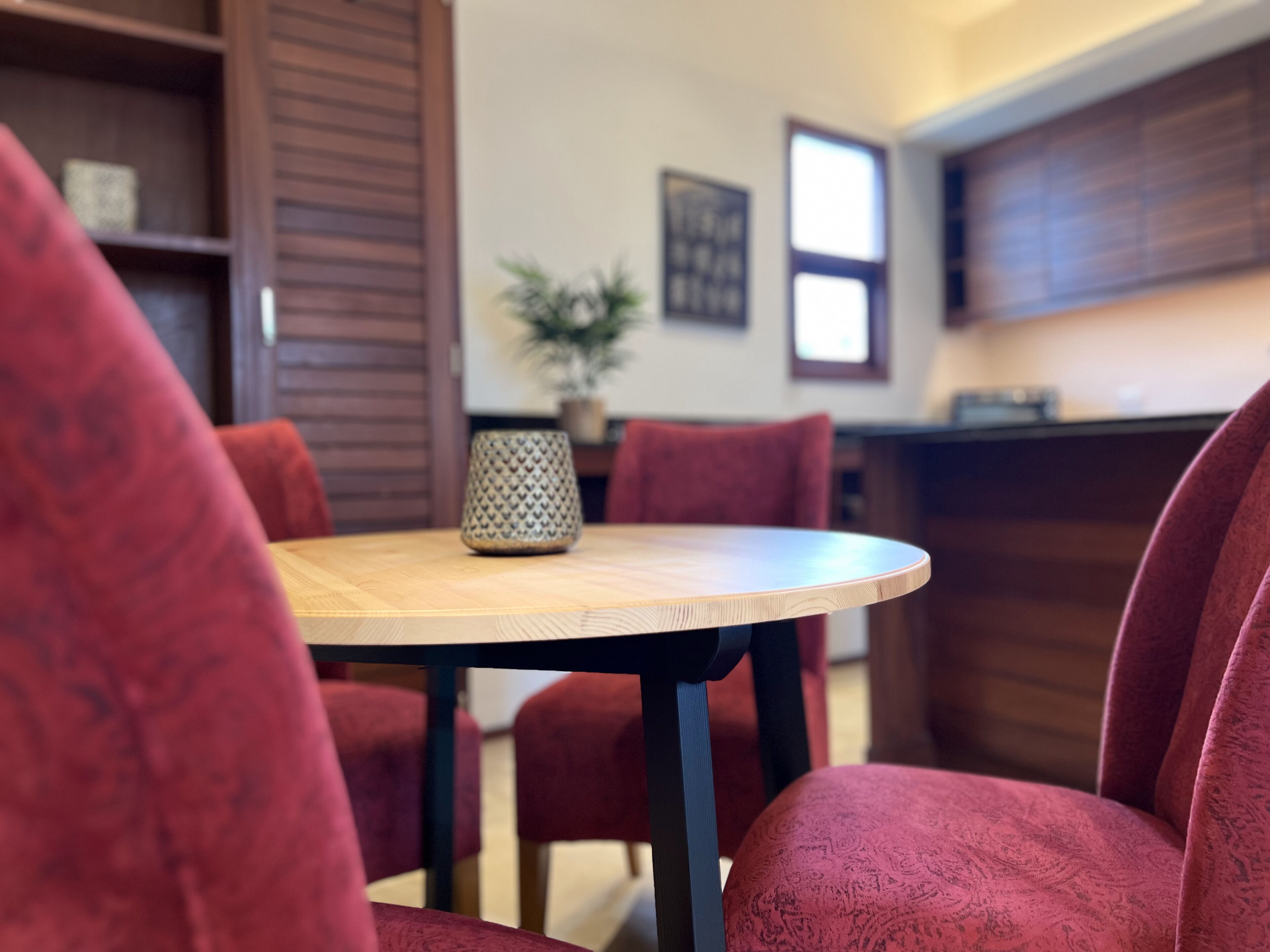 A dining area with a round table, red upholstered chairs, a patterned vase, and a potted plant.