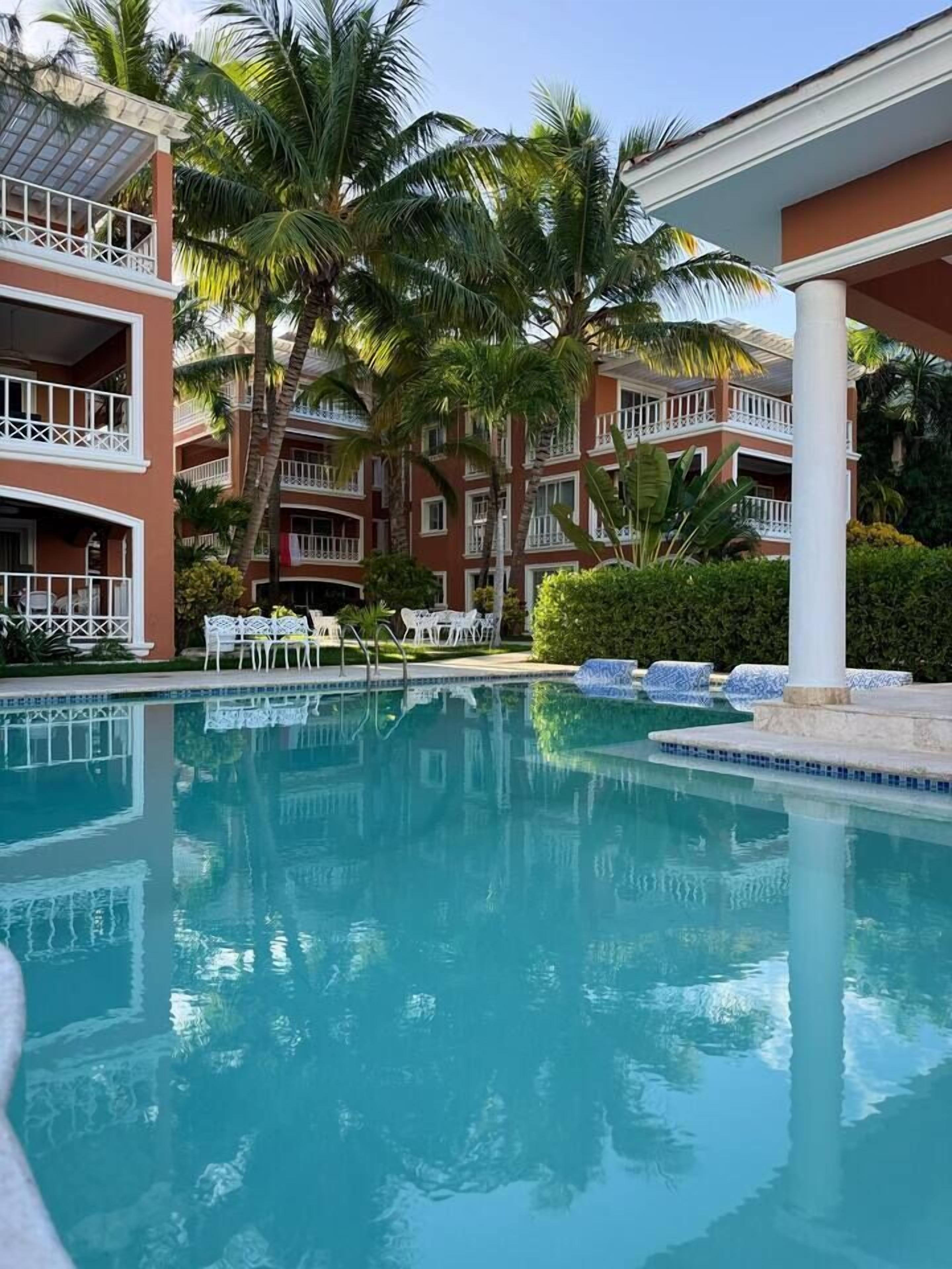 A hotel with a swimming pool, palm trees, and a two-story building with balconies.