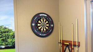 Un jeu de fléchettes, des queues de billard et un porte-billes dans un coin de la pièce.