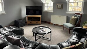 Un salon avec un canapé en cuir, une table basse, un téléviseur posé sur un meuble en bois et une fenêtre donnant sur des immeubles.