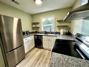A modern kitchen with stainless steel appliances, a dishwasher, a washing machine, and granite countertops. - Historic District Retreat - Newly Renovated 2BR (Palmetto)