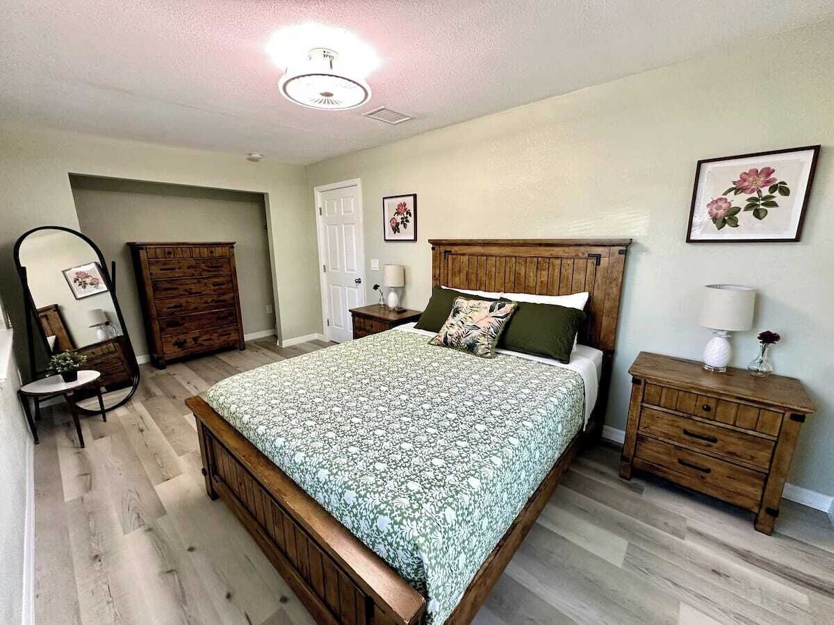 A bedroom with a wooden bed, a dresser, a nightstand, a mirror, and a door.