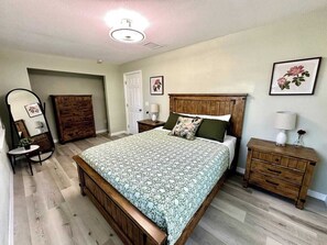 A bedroom with a wooden bed, a dresser, a nightstand, a mirror, and a door. - Historic District Retreat - Newly Renovated 2BR (Palmetto)