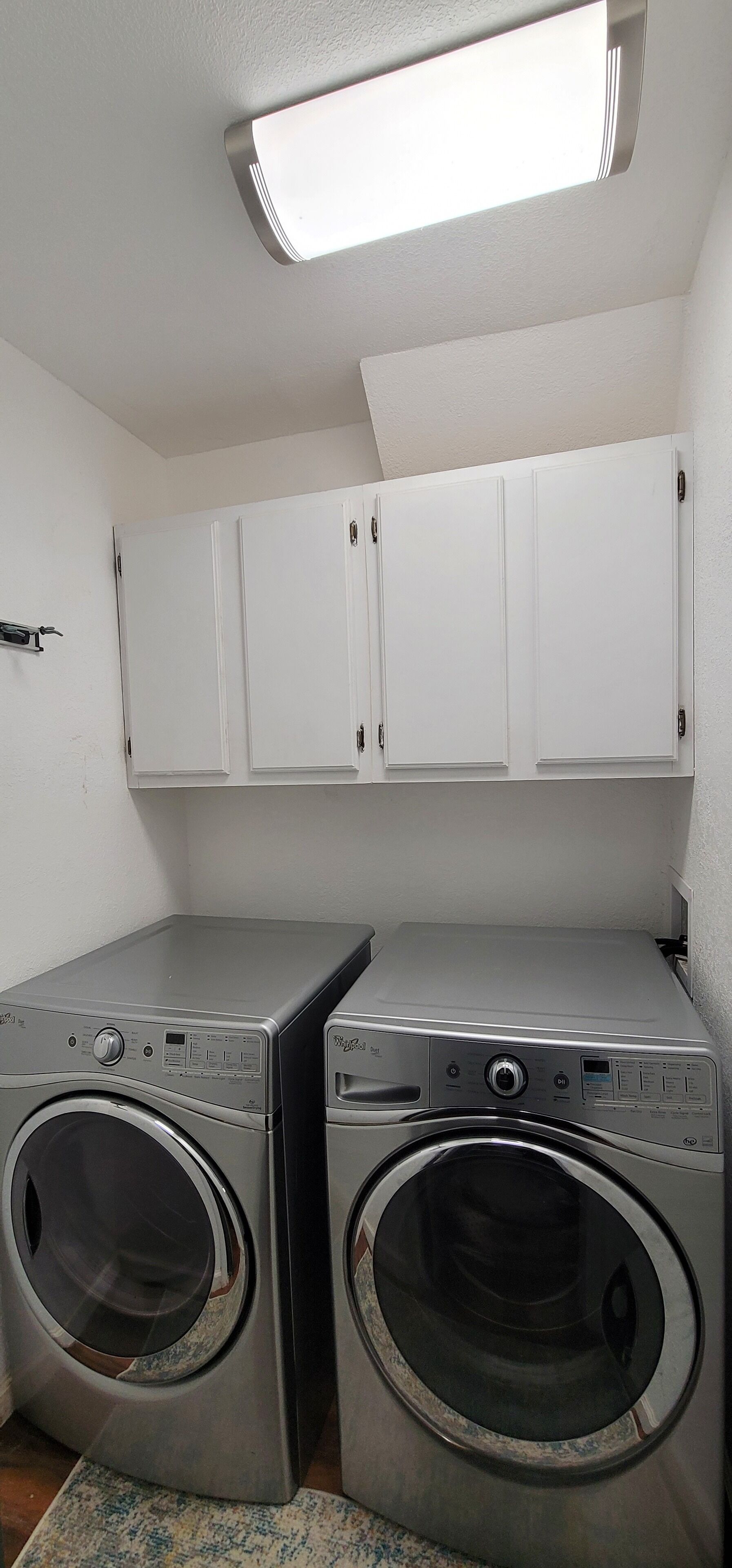 A laundry room with two front-loading washing machines, white cabinets above, and a ceiling light.