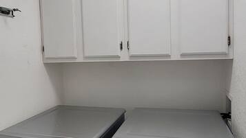 A laundry room with two front-loading washing machines, white cabinets above, and a ceiling light.