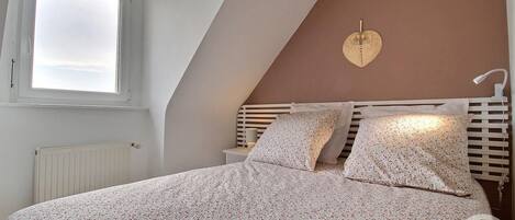 A bedroom with a sloped ceiling, a bed with floral bedding, a bedside lamp, and a window with blinds.