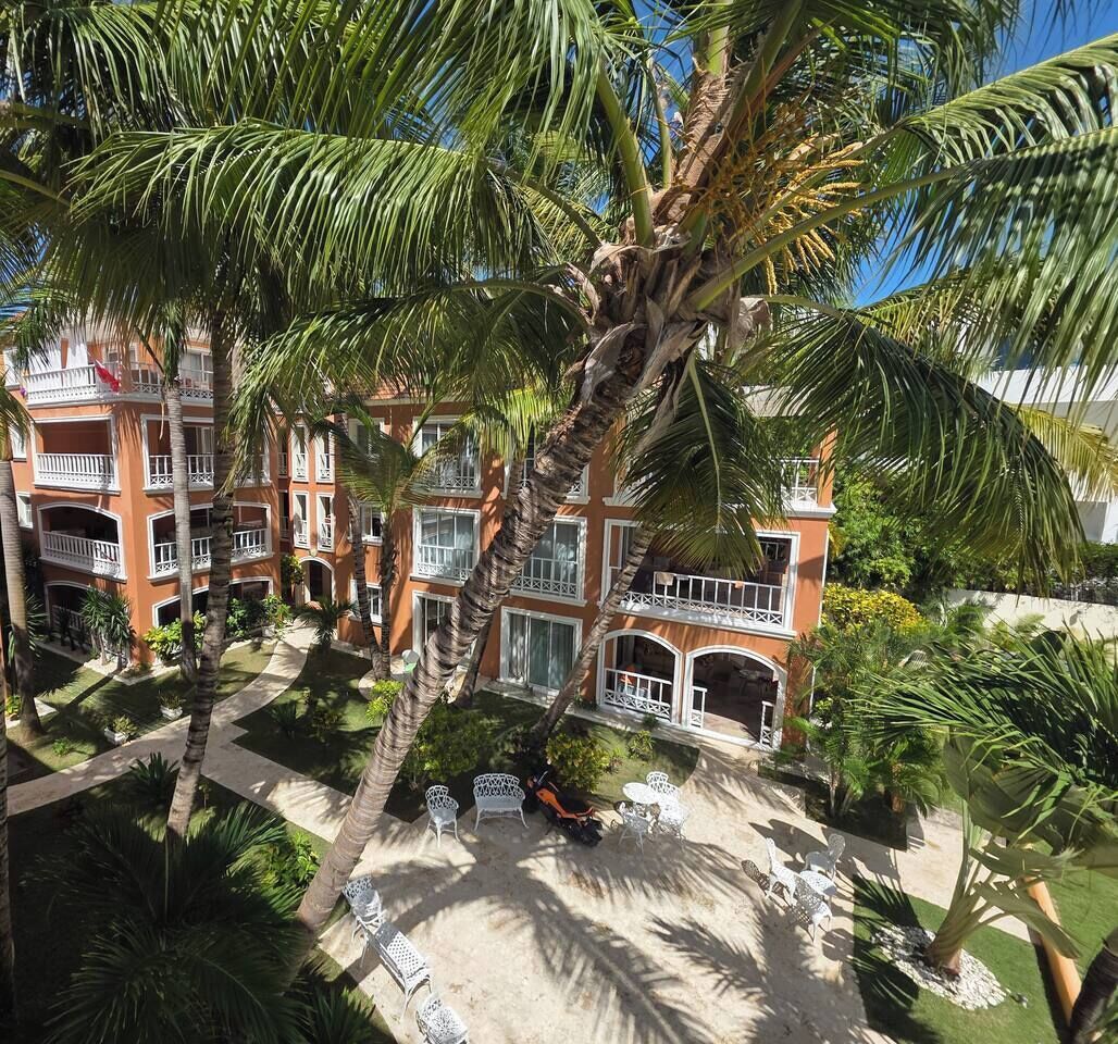 Een hotel met meerdere verdiepingen, balkons, palmbomen en buitenzitplaatsen.