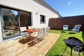 Eine Terrasse mit Tisch und Stühlen, einem Grill und einem Rasenbereich mit Liegestühlen.