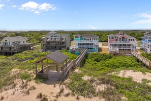 A beachfront property with multiple houses, a wooden deck, and a beach view. - 6099-Turquoise Turtle - Nags Head Oceanfront | Pool, Hot Tub & Sleeps 16 (Nags Head)