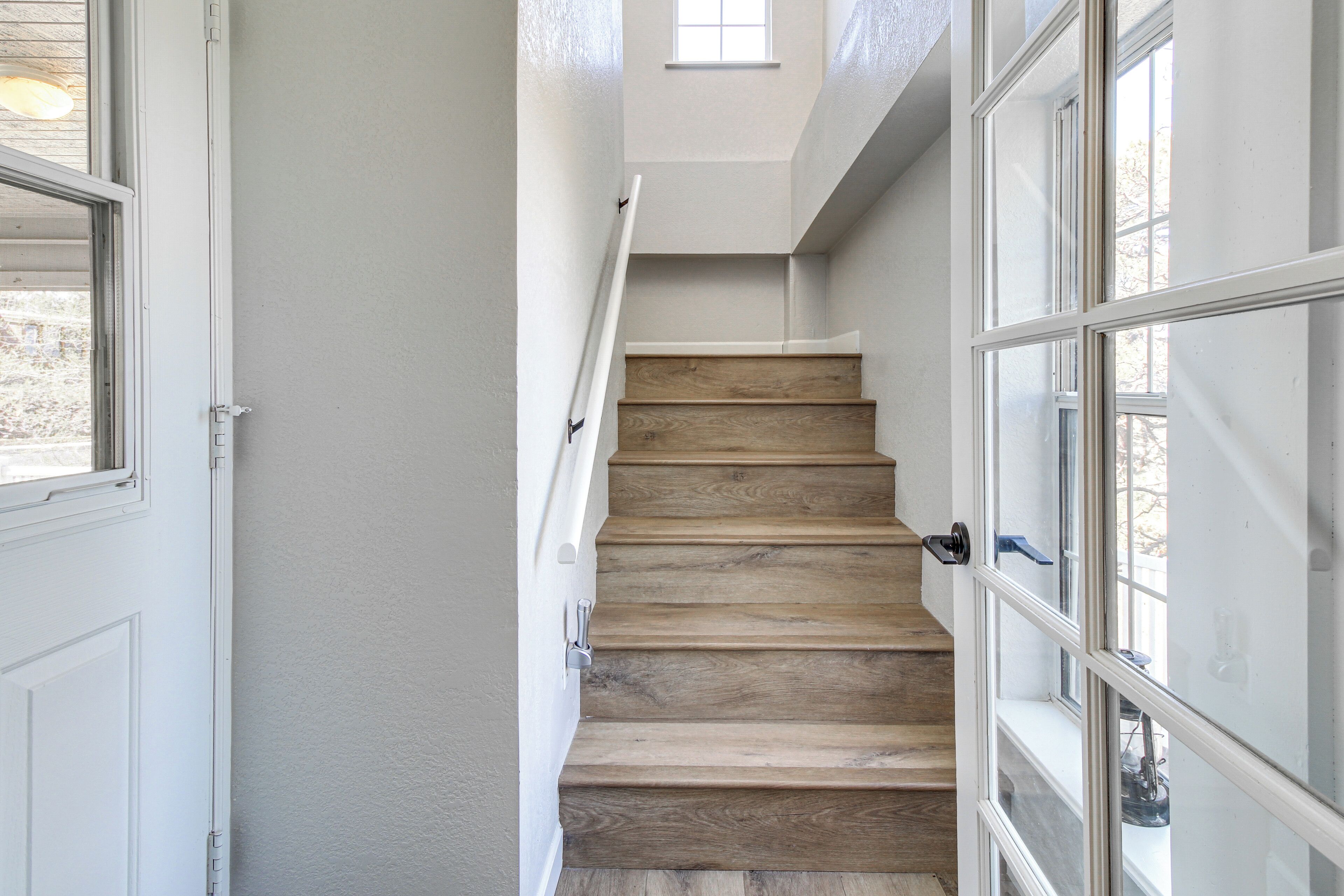 Un escalier avec des marches en bois et des murs blancs, menant à un palier doté d’une fenêtre.