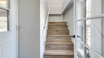 Un escalier avec des marches en bois et des murs blancs, menant à un palier doté d’une fenêtre.