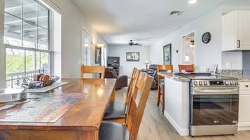 Une cuisine spacieuse avec une table à manger en bois, des chaises, un grand îlot central doté d’un four et un téléviseur.